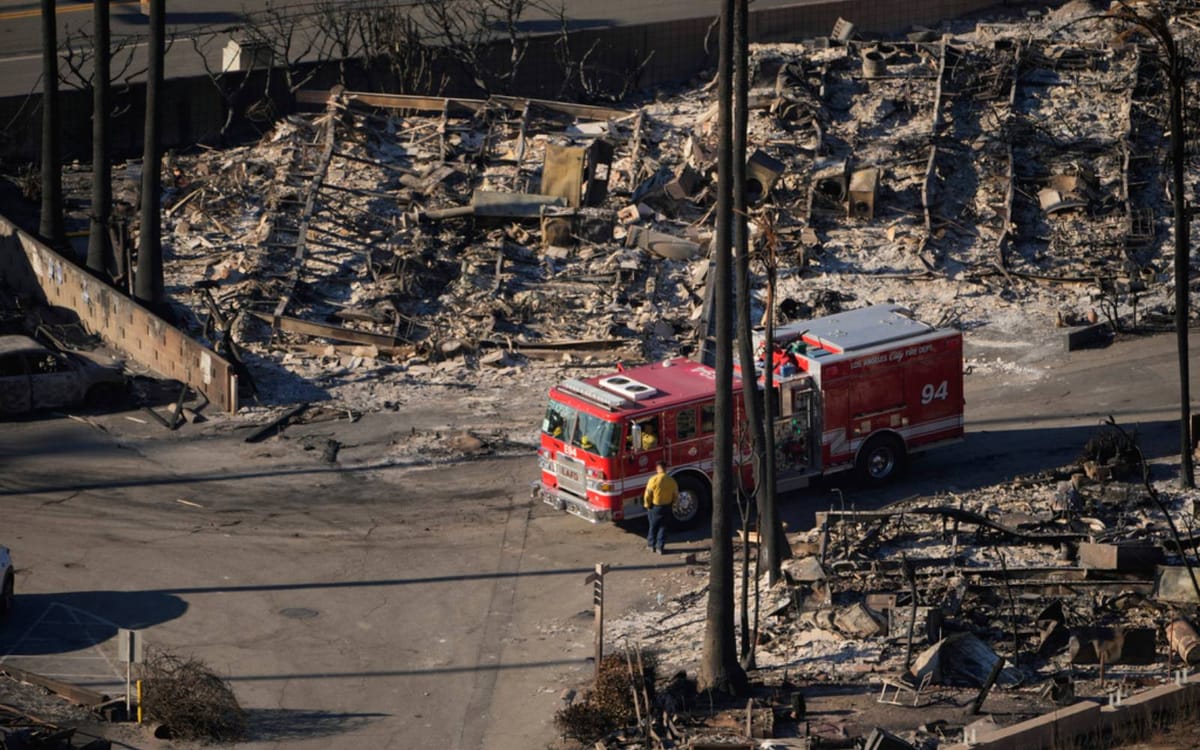 a picture of a bright red fire engine sitting in front of the shells of a number of burned out houses, all in grey rubble